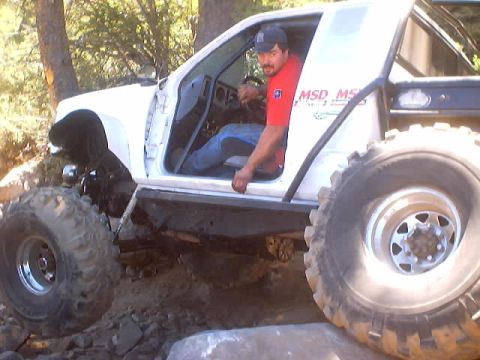 1976 Ford F-100 - A white off-road truck navigates rocky terrain with its driver visible.