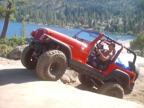 1976 Ford F-100 - Off-road Jeep navigates a challenging trail with a scenic lake and forest in the background.