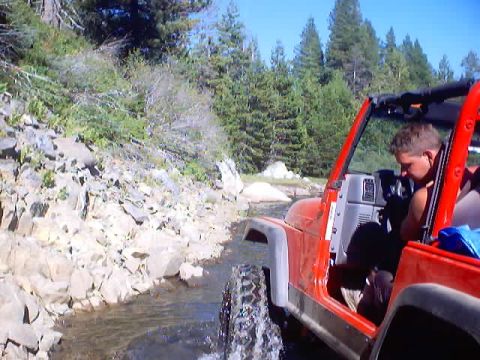 1976 Ford F-100 - Red Jeep Wrangler navigates a shallow stream on a wooded trail.