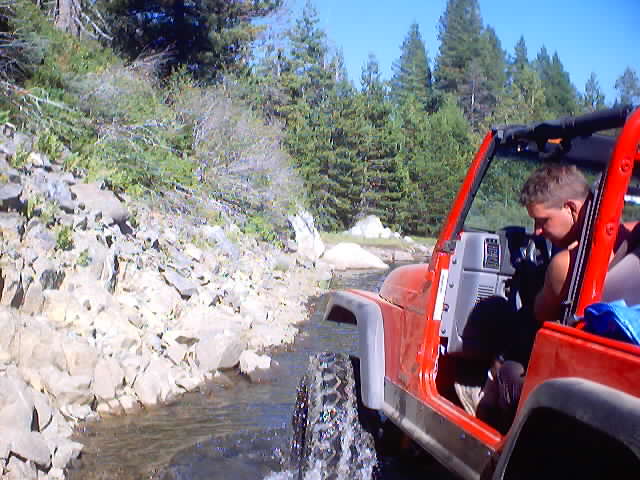 Red Jeep Wrangler driving through a rocky stream with a person in the driver's seat