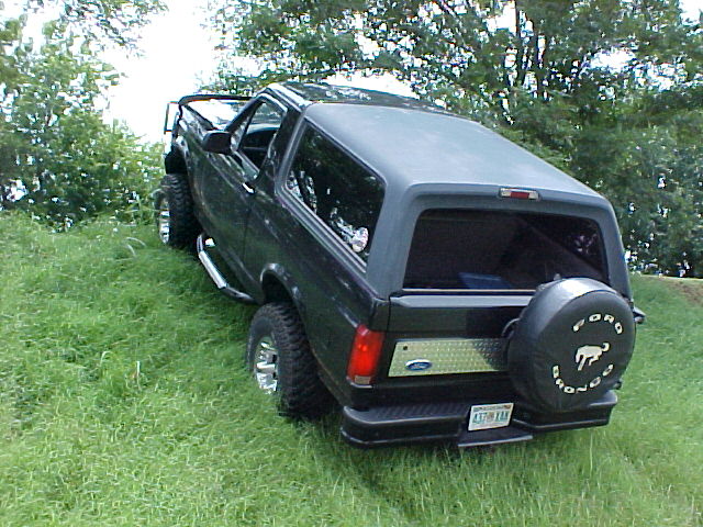 Black lifted Ford Bronco rear view with Ford Bronco spare tire cover on grass hill