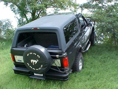 1995 Ford Bronco - This black Ford Bronco is parked on a grassy incline with trees in the background.