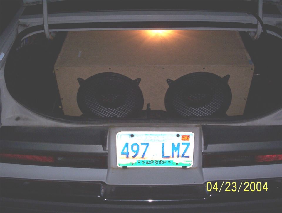 Car trunk with carpeted ported subwoofer box and two subs, lit license plate 497 LMZ, date 04/23/2004