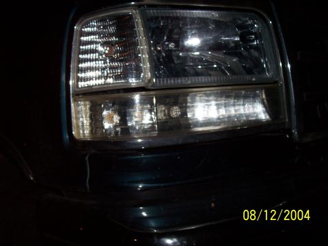 1994 Ford Bronco - Close-up of the headlight assembly on a dark green 1992 Ford F-150, with a date stamp visible.