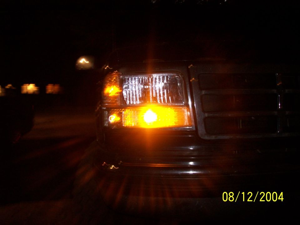 Night close-up of a Ford truck's lit amber turn signal beside the headlight and grille