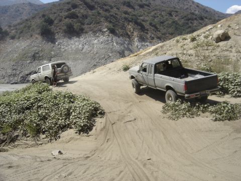1988 Ford Bronco - A 1988 Ford Bronco navigates a dusty, mountainous terrain alongside a pickup truck.