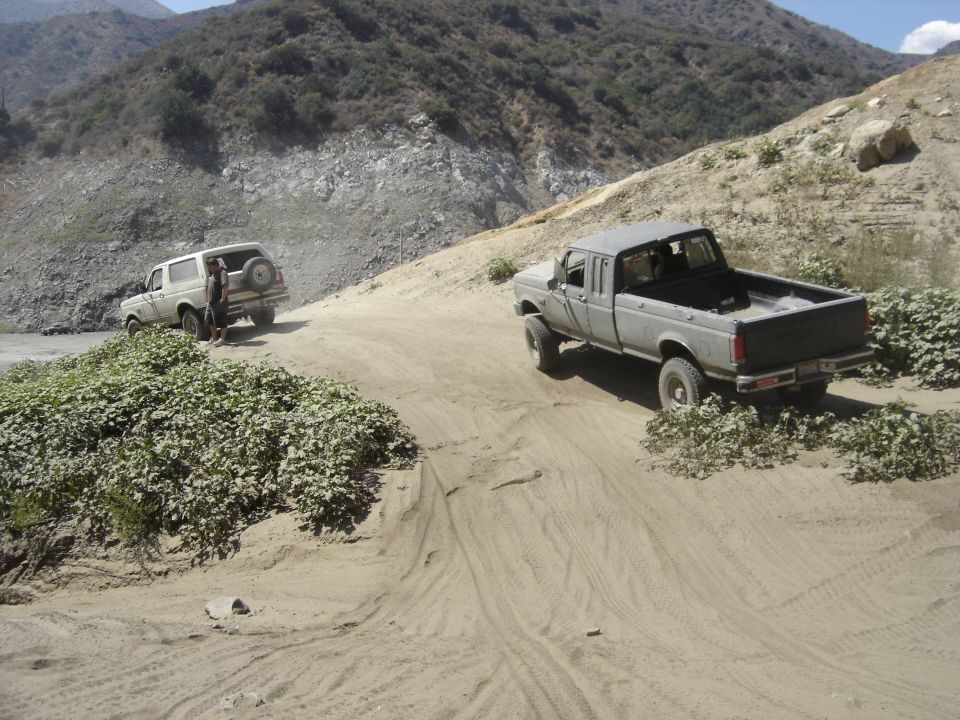 Dusty lifted white Ford extended-cab pickup and a Bronco parked in a sandy desert wash