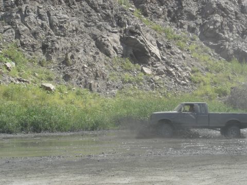 1988 Ford Bronco - A Ford pickup truck navigates a muddy terrain, creating a splash as it moves through the mire.