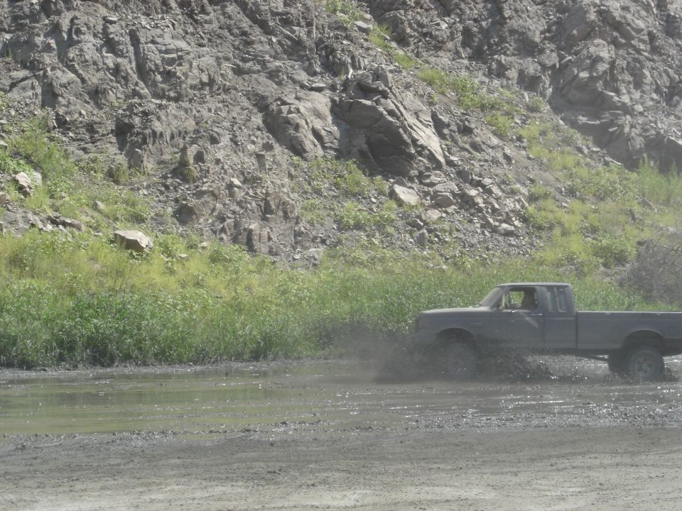 Lifted dark blue Ford pickup on mud tires splashing through a water hole in a quarry