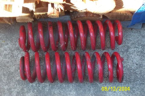 1996 Ford Bronco - Pair of red coil springs shown on a concrete surface with stacked wood behind them.