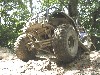 1992 Ford Bronco - This off-road vehicle is covered in mud, navigating a rough terrain with trees surrounding it.