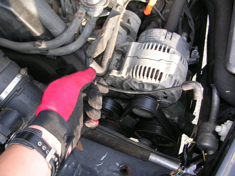 Close-up of a car engine with a hand in a red glove working on the alternator and belts