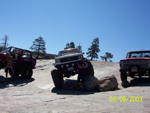 1976 Ford F-100 - Three modified off-road trucks are parked on a rocky surface under a clear blue sky.