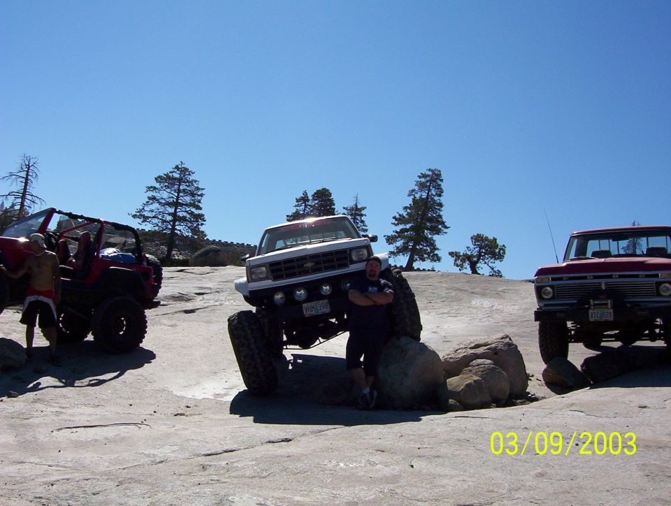 Red 1976 Ford F-100 parked on rocks with two other off-road vehicles