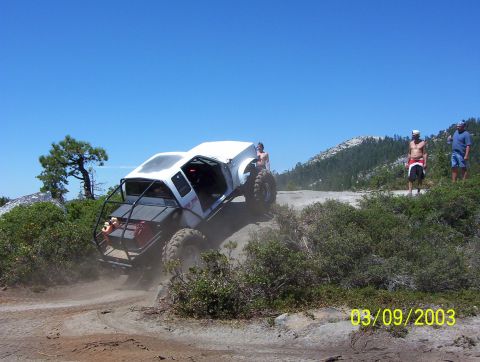 1976 Ford F-100 - An off-road vehicle navigates a dusty trail with spectators watching on a sunny day.