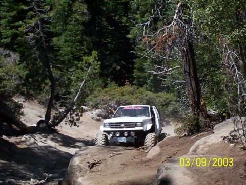 1976 Ford F-100 - A white off-road truck tackles a challenging rocky path in a wooded area.