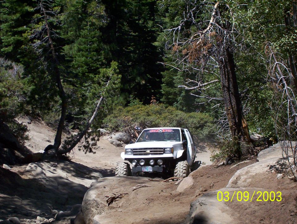 White off-road truck with large tires navigating a rocky trail