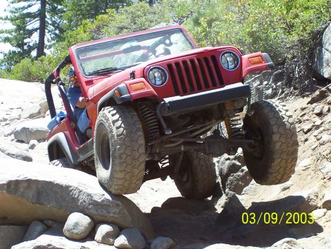 1976 Ford F-100 - A red Jeep Wrangler tackles a challenging rocky off-road course, demonstrating its suspension and tire grip.