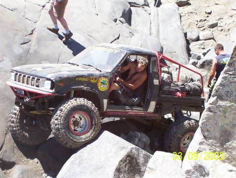 1976 Ford F-100 - A modified truck navigates a challenging rocky terrain, with people observing the action.