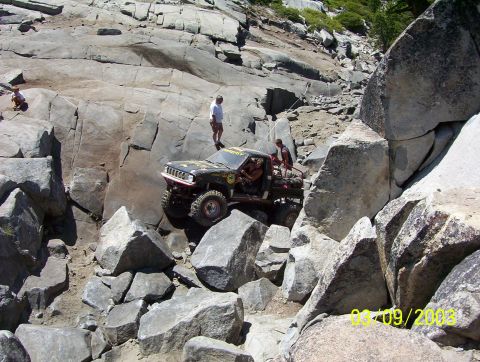 1976 Ford F-100 - An off-road vehicle tackles a challenging rocky terrain with people observing.