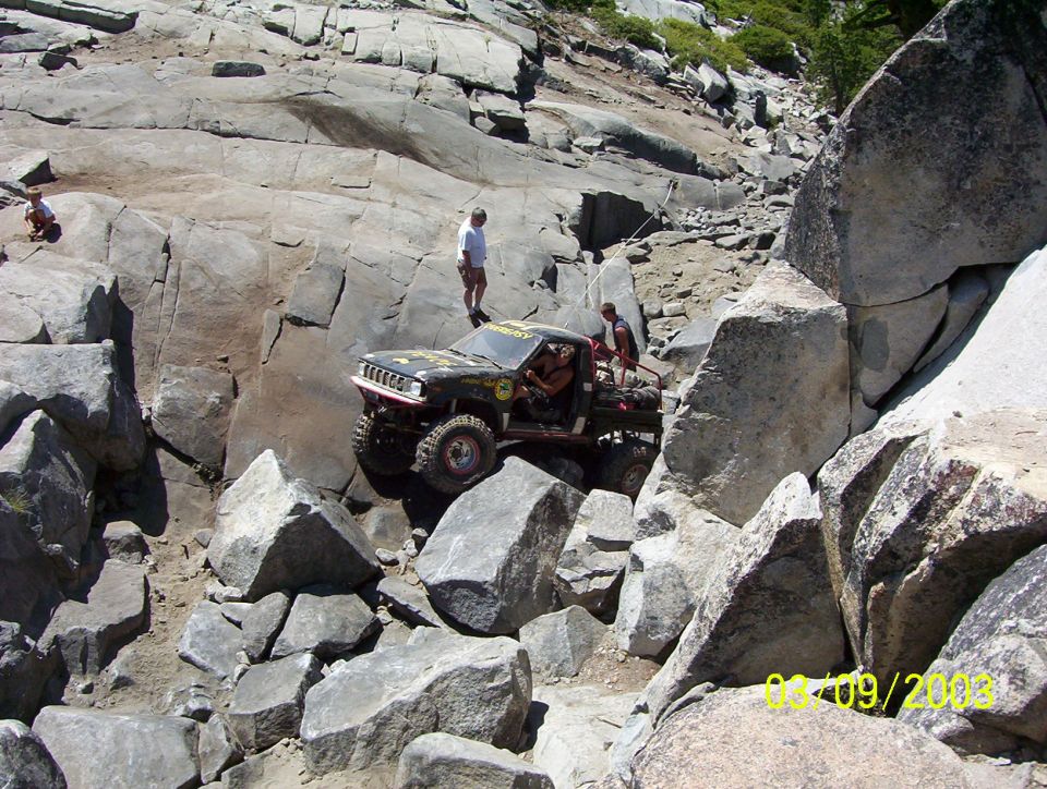 Black off-road vehicle with lifted suspension navigating a rocky incline