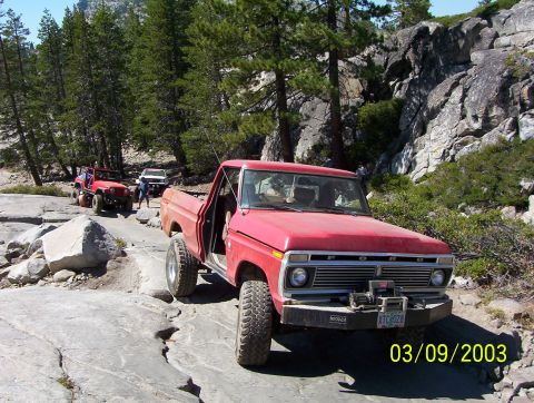 1976 Ford F-100 - A red 1976 Ford F-100 navigates a rocky trail, with other off-road vehicles visible in the background.