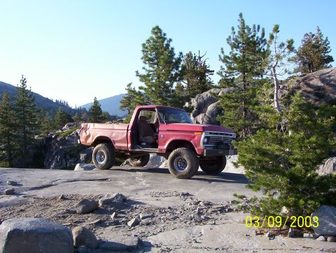 1976 Ford F-100 - A red pickup truck is parked on a large rock in a mountainous, wooded area.