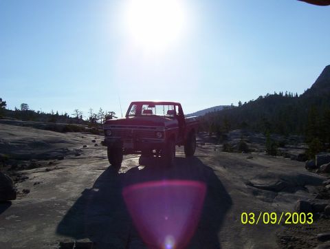 1976 Ford F-100 - A red pickup truck is parked on a rocky terrain under a bright sun.
