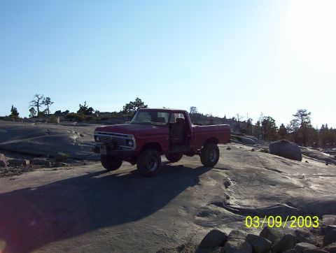 1976 Ford F-100 - A red 1975 Ford F-100 pickup truck is parked on a rocky terrain with trees in the background.