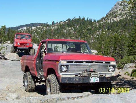 1976 Ford F-100 - Two off-road vehicles, a red Ford F-100 and a red Jeep Wrangler, navigate a rocky mountain path.