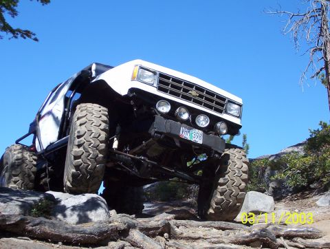 1976 Ford F-100 - A heavily modified white truck navigates a rocky trail under a clear blue sky.