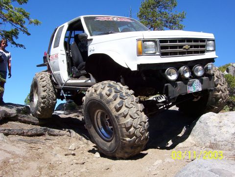 1976 Ford F-100 - Modified SUV with oversized tires navigates a rocky trail under a clear blue sky.