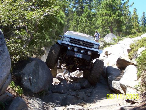 1976 Ford F-100 - A modified truck is shown crawling over large rocks on a steep, wooded trail.
