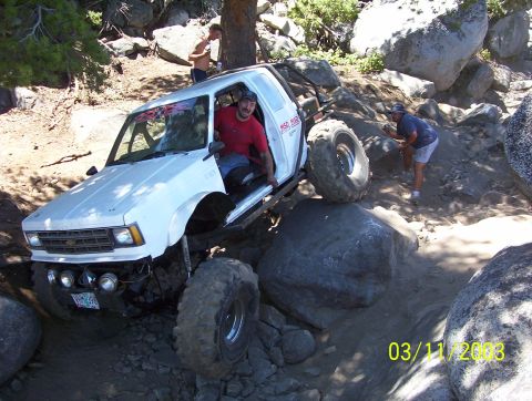 1976 Ford F-100 - A white doorless Chevrolet S-10 rock crawler with an exo cage, tube rock sliders and MSD decals climbs over granite boulders on a mountain…