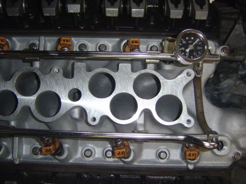 1993 Ford Bronco - Close-up of a V8 lower intake manifold with the upper plenum removed, showing machined runner openings, stainless fuel rails, orange-connec…