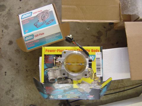 1993 Ford Bronco - A new BBK Power-Plus Series billet aluminum throttle body with attached IAC valve and throttle position sensor, laid on its yellow retail b…