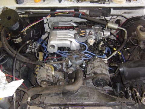 1993 Ford Bronco - Overhead shot into an engine bay with a Ford 5.0 Liter Cobra upper intake manifold installed on the V8, blue spark plug wires routed to the…