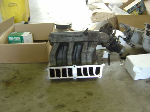 1993 Ford Bronco - A removed, grimy stock upper intake manifold standing on a shop floor with its eight-port mating flange facing the camera, the old gasket s…