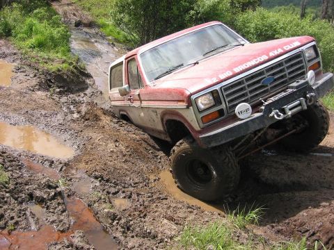 1985 Ford Bronco - This red 1980s Ford Bronco, part of the "BIG BRONCOS 4X4 CLUB", navigates a challenging muddy trail.