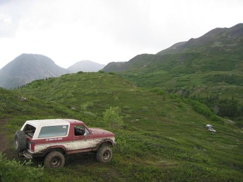 1985 Ford Bronco - A 1985 Ford Bronco navigates a , green mountain terrain under an overcast sky.