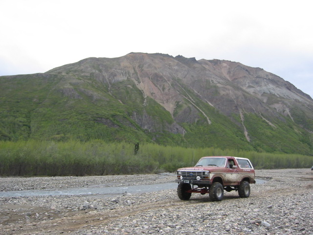 1985 Ford Bronco parked on a rocky riverbed with a large mountain in the background