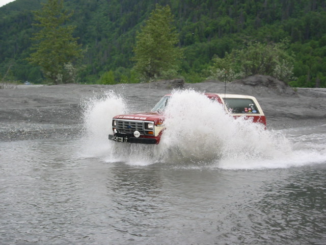Red and white SUV splashing through water, front grille visible
