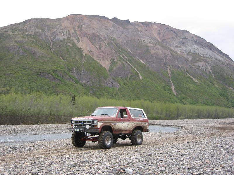 red lifted Ford Bronco parked on a rocky riverbed with a mountain in the background
