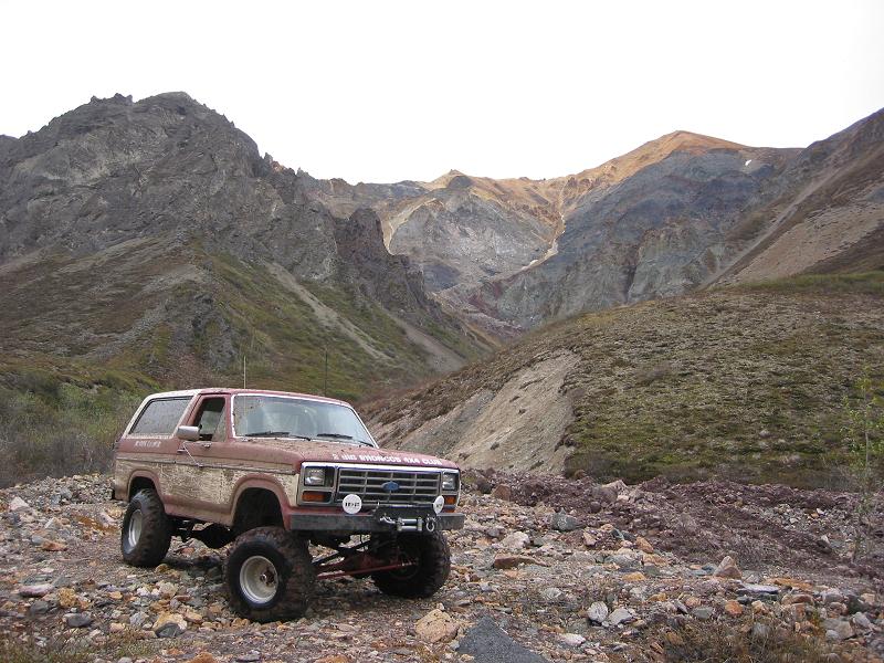 Lifted red and white Ford Bronco with winch bumper parked on rocks below barren mountains