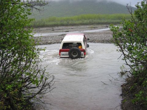 1985 Ford Bronco - A red and white Ford Bronco navigates a water crossing in a natural landscape.