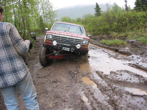 1985 Ford Bronco - A red Ford Bronco navigates a muddy off-road trail, demonstrating its off-road capabilities.