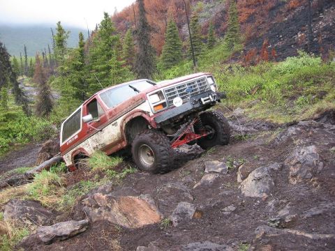 1985 Ford Bronco - Ford Bronco navigating a difficult off-road trail with steep inclines and loose terrain.