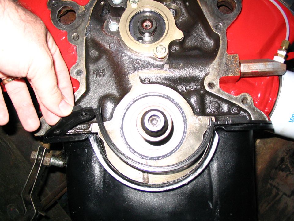 Engine front with timing cover off, crankshaft and oil pump exposed, hand at left