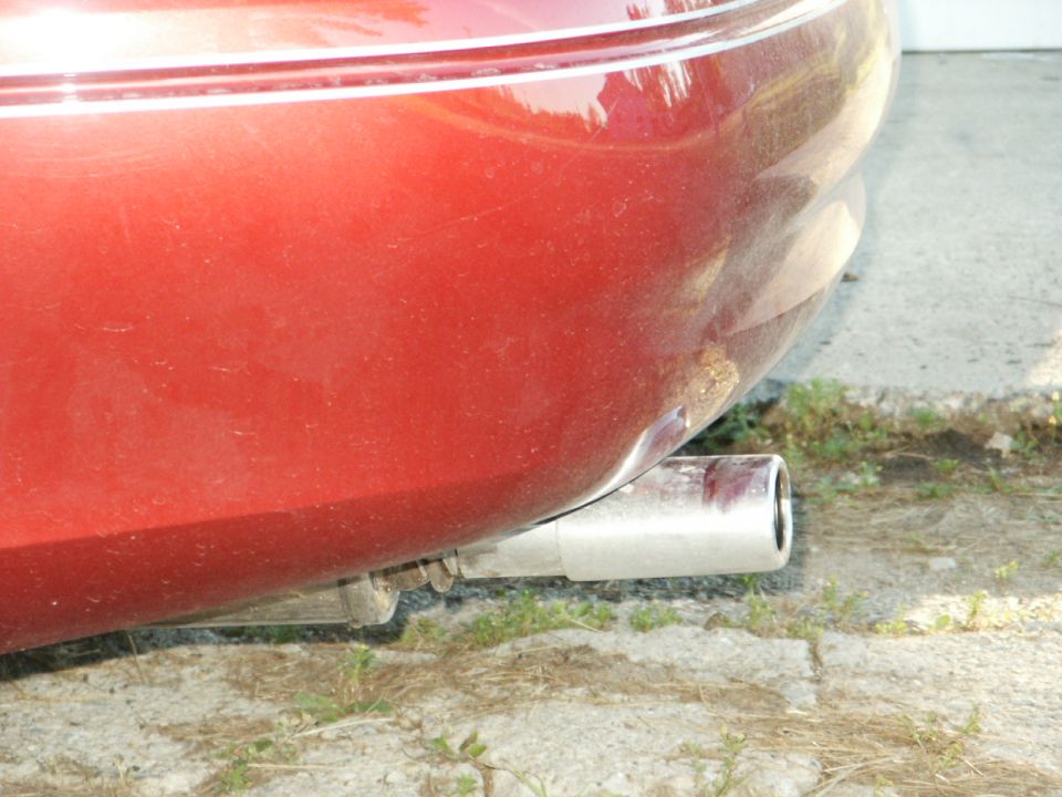 Close-up of a red car's rear bumper and exhaust pipe. Text at bottom reads SUPERMOTORS