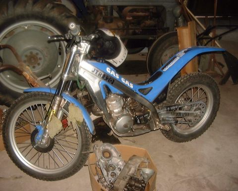 1985 Ford F-150 - A blue and silver dirt bike is parked indoors, with a tractor in the background and engine parts in a box.